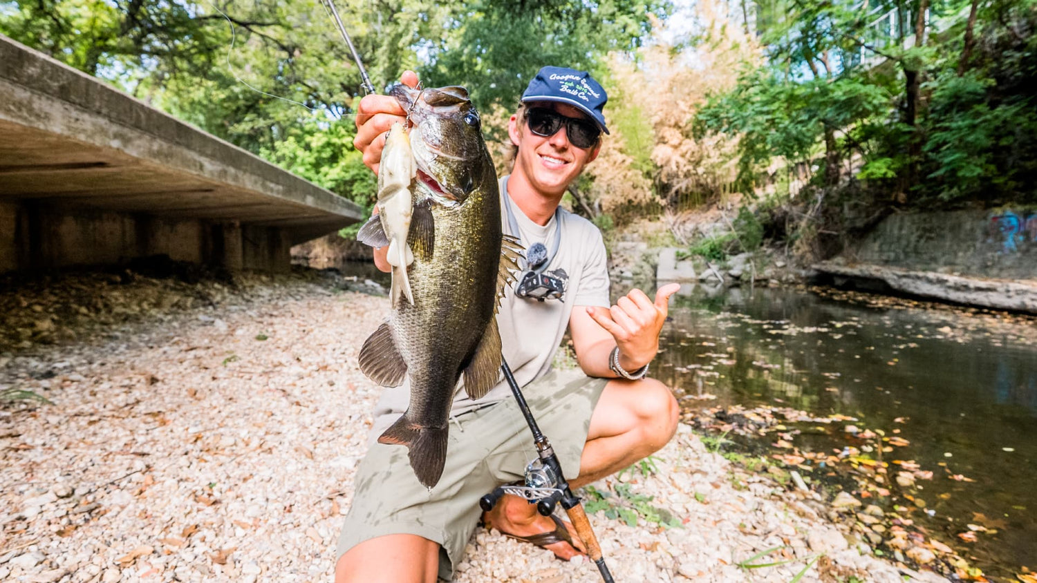 Angler holding largemouth bass caught in shallow creek water