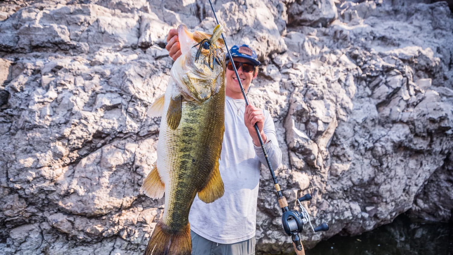angler holding largemouth bass caught on a jig near rocky river bank
