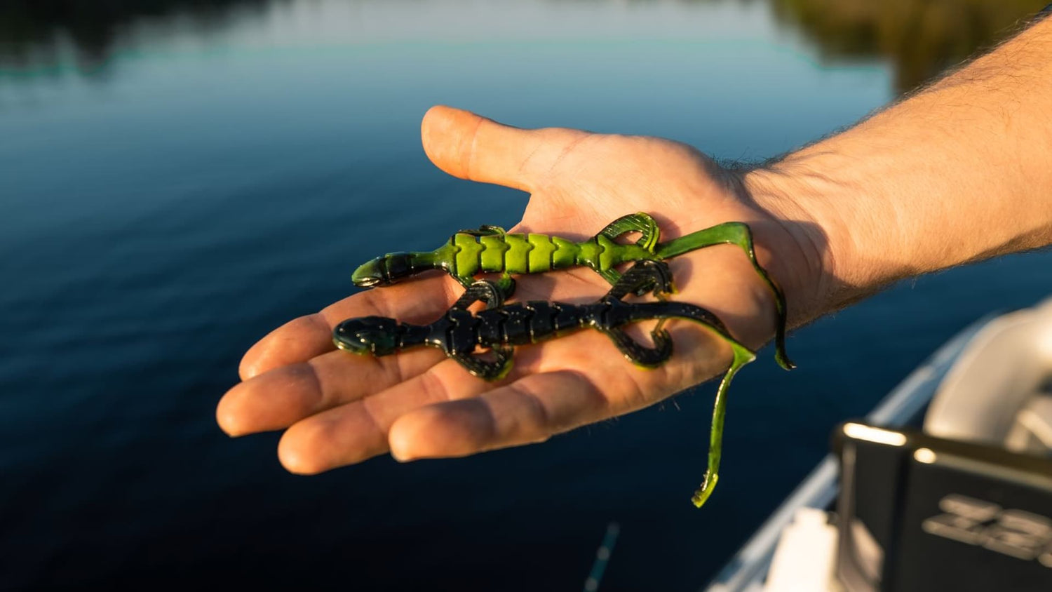 Hand holding soft plastic lizard baits over water from boat